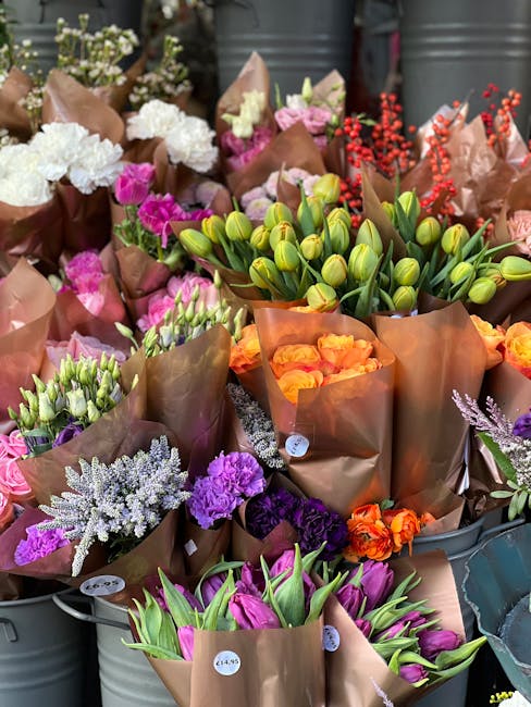 An assortment of fresh flower bouquets wrapped in brown kraft paper, featuring a variety of blooms including pink tulips, orange roses, purple statice, white astilbe, green tulip buds, and red berries
