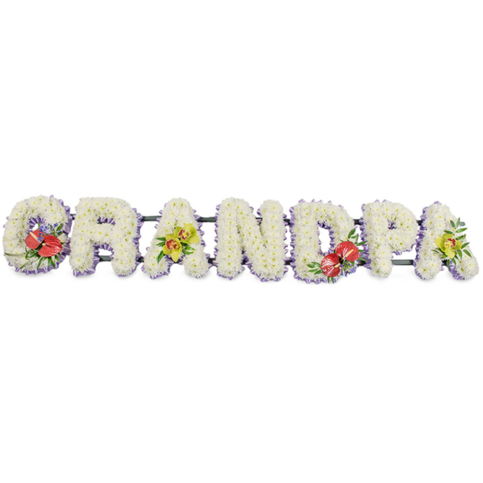 This image shows a striking floral letter tribute arranged to read "GRANDPA" in large, block capitals, carefully positioned against a bright white background that highlights every petal and curve. Each letter is fully covered with small, pristine white chrysanthemums, the blooms packed so densely that no gaps are visible, creating a smooth, velvety surface reminiscent of freshly fallen snow. The chrysanthemums' subtle texture gives the design depth and softness, conveying purity, peace, and the gentlest kind of goodbye. At the base of each letter, a fine band of lavender or soft purple ribbon peeks out, framing the white blooms with a delicate shadow of colour and lending the design a polished, considered finish. The letters are mounted on sturdy dark green bars that run horizontally beneath them, providing unseen support while allowing the word to appear as one continuous, flowing tribute. Carefully placed accent sprays bring moments of vibrant colour and emotion: on the left-hand 'G' and the central 'D', clusters of deep red anthuriums with their glossy, heart-shaped surfaces and distinctive central spadices nestle among rich green foliage, echoing feelings of deep affection and remembrance. On the first 'A' and the final 'A', graceful stems of yellow-green orchids, likely cymbidium, arch across the white flowers, their luminous, almost citrusy hue adding a refined brightness and a sense of lasting admiration. The composition feels calm and dignified, suitable for a funeral service or celebration of life for a beloved grandfather in Rotherhithe, perhaps travelling from a local florist on Lower Road to a chapel by the river. It is a bespoke memorial piece that speaks of honour, gratitude, and the enduring bonds of family.