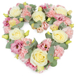 A softly coloured heart-shaped funeral wreath is shown against a crisp white backdrop, its densely packed flowers forming a complete, rounded heart that feels both comforting and refined. At the core of the design are generous cream and pale buttery-yellow roses, their tightly layered petals opening into full, cup-shaped blooms that suggest warmth and devotion. These are surrounded and supported by clusters of delicate pastel pink carnations, each cluster a mass of tiny ruffled petals that lend a feathery softness to the overall look. Threaded between them are lisianthus blooms in deeper rose and mauve-pink shades, their looser, more open flowers providing contrast and a sense of gentle movement, like a soft breeze passing through a quiet corner of Rotherhithe Village. Fresh eucalyptus foliage in cool, silvery-green tones arcs through the heart, its rounded leaves creating a subtle frame and adding an airy, natural grace to the compact design. Small, yellowish-green buds dot the arrangement like whispered notes of hope, balancing the themes of loss and remembrance. The colour palette of cream, pink, and muted green feels peaceful, similar to an early morning walk by the Thames Path near Canada Water, when the light is soft and the world is hushed. Every element speaks of care and intention, as though arranged by a local Rotherhithe florist for a funeral, memorial, or celebration of life. This heart-shaped tribute quietly conveys love, sympathy, and cherished memories, offering a gentle way to say goodbye when words are not enough.